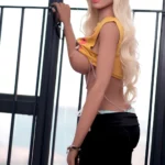 Charlotte Sex Doll 165cm Bonnet F en pose debout, tenue jaune et noire, cheveux blonds ondulés.