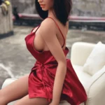Ambre Sex Doll 165cm Bonnet F 6ye Premium en robe rouge, assise sur un canapé extérieur.