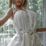 Océane Sex Doll 165cm Bonnet F en robe blanche, posant près d'une fenêtre lumineuse.