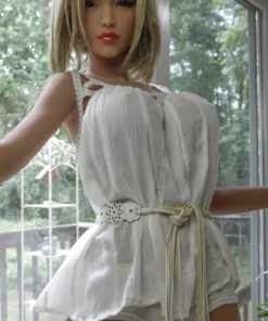 Océane Sex Doll 165cm Bonnet F en robe blanche, posant près d'une fenêtre lumineuse.