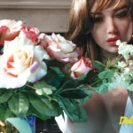 Riley Sex Doll 150cm Bonnet D 6ye Premium posée près d'un bouquet de roses.
