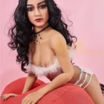 Alicia Sex Doll 150 cm IronTech posée sur un coussin rouge, cheveux noirs bouclés.