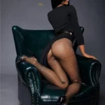Alicie Sex Doll 168 cm en pose à genoux sur fauteuil, tenue noire élégante, vue arrière.
