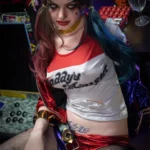 Amara Sex Doll 166 cm IronTech en tenue colorée, assise, cheveux bicolores, maquillage accentué.