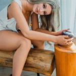 Amberlina Sex Doll 164 cm IronTech assise, cheveux blonds, robe blanche, bottes marron.