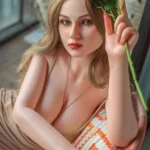 Amélie Sex Doll 165 cm IronTech, posée sur un canapé, tenant des roses, robe beige.