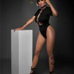 Amova Sex Doll 165 cm IronTech Doll en tenue noire, pose debout élégante près d'un socle.