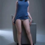 Anabelle Sex Doll 166 cm en robe bleue, posée debout contre un fauteuil, cheveux bruns courts.