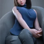Anabelle Sex Doll 166 cm IronTech posée assise, vêtue d'un pull bleu et jeans, cheveux bruns.