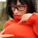Aurabella Sex Doll 167 cm posée contre un arbre, portant un pull rouge et des lunettes noires.