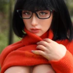 Aurabella Sex Doll 167 cm en pull rouge, regard intense, lunettes noires, extérieur.