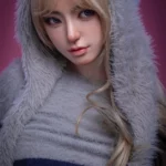 Avalyn Sex Doll 164 cm IronTech, gros plan visage, capuche en fourrure, cheveux blonds.
