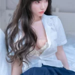 Bellora Sex Doll 168 cm IronTech Doll en chemise blanche et jupe bleue, assise sur un lit.