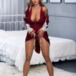 Dollya Sex Doll 165 cm IronTech en robe rouge, debout devant un lit, cheveux longs et blonds.