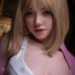 Ellya Sex Doll 169 cm IronTech en pose assise, cheveux blonds, débardeur blanc, veste rose.