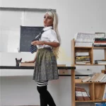 Emmarose Sex Doll 150 cm IronTech Doll TPE en tenue d'écolière, debout près d'une bibliothèque.
