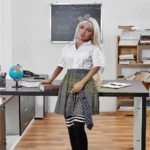 Emmarose Sex Doll 150 cm IronTech en tenue d'écolière, debout près d'un bureau.