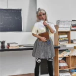 Emmarose Sex Doll 150 cm IronTech Doll TPE en tenue d'écolière, debout dans une bibliothèque.