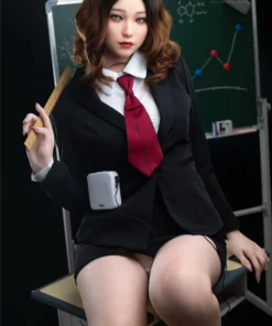 Joliebelle Sex Doll 166 cm posée assise, tenue d'écolière, règle en main, devant tableau.