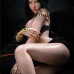 Lilika Sex Doll 166 cm IronTech en pose assise, parée de bijoux dorés et émeraudes.