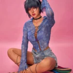 Lilun Sex Doll 168 cm IronTech, assise sur skateboard, chemise bleue, fond rose.
