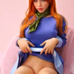 Lizette Sex Doll 167 cm, assise, robe bleue, cheveux roux, fond rose, IronTech Doll.