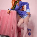 Lizette Sex Doll 167 cm IronTech en pose inclinée, robe bleue, collants blancs, fond rose.
