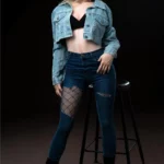 Lolita Sex Doll 168 cm IronTech, pose debout, veste en jean, jeans déchiré, fond sombre.