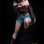Loraline Sex Doll 165 cm IronTech en tenue cowgirl, assise sur un tabouret, tenant un pistolet.