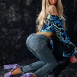 Lovabelle Sex Doll 167 cm en pose accroupie, chemisier bleu, jeans moulant, talons violets.