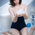 Luluza Sex Doll 168 cm en maillot bleu, tenant de la mousse devant une baignoire blanche.