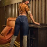 Luméa Sex Doll 165 cm IronTech en pose debout, jeans moulant, chemise marron, ambiance boisée.