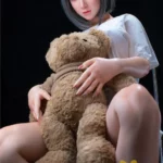 Lumiria Sex Doll 165 cm IronTech, assise avec ours en peluche, cheveux gris, fond noir.