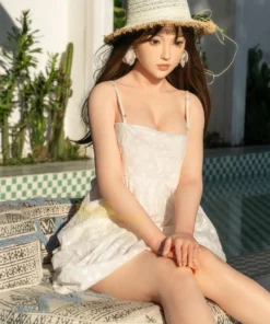 Ninabelle Sex Doll 166 cm IronTech en robe blanche et chapeau, assise près d'une piscine.