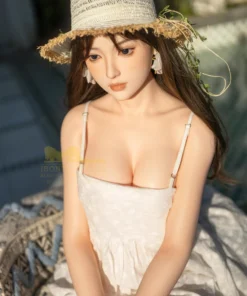 Ninabelle Sex Doll 166 cm en robe blanche, chapeau de paille, assise en extérieur.