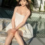 Ninabelle Sex Doll 166 cm IronTech en robe blanche, assise au soleil, chapeau en paille.