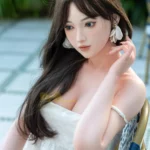 Ninabelle Sex Doll 166 cm IronTech en robe blanche, assise, regard pensif, cheveux longs.