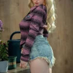 Serenzia Sex Doll 165 cm IronTech en short en jean, pose de profil, fond intérieur bois.