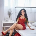 Zadie Sex Doll 150 cm IronTech en robe rouge, assise sur un lit, cheveux noirs longs.