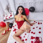 Zadie Sex Doll 150 cm IronTech Doll TPE allongée sur lit, pétales rouges, lingerie rouge.