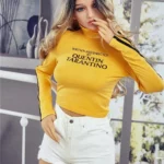 Alicine Sex Doll 163 cm IronTech, debout en short blanc et haut jaune, intérieur moderne.