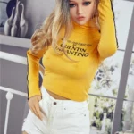 Alicine Sex Doll 163 cm IronTech Doll TPE en tenue décontractée, pose assise sur lit.