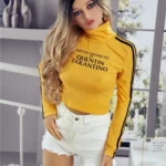 Alicine Sex Doll 163 cm IronTech en pull jaune et short blanc, debout dans une chambre.