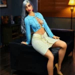 Alyona Sex Doll 164 cm IronTech, assise sur canapé, tenue bleue et jupe beige.