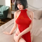 Amecha Sex Doll 165 cm IronTech en robe rouge, assise sur un lit, cheveux courts noirs.