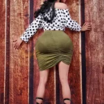 Amelia Sex Doll 160 cm IronTech en jupe verte, pose de dos contre un mur en bois.
