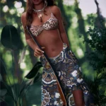 Amorable Sex Doll 175 cm IronTech en tenue exotique, pose debout en extérieur tropical.
