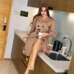 Amoryle Sex Doll 163 cm IronTech Doll en trench beige, assise sur un comptoir de cuisine moderne.
