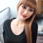 Aurélie Real Doll 165 cm IronTech Doll TPE, cheveux longs bruns, robe noire, ambiance intérieure.