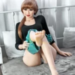 Aurélie Real Doll 165 cm IronTech Doll TPE assise sur lit, robe noire, cheveux longs.